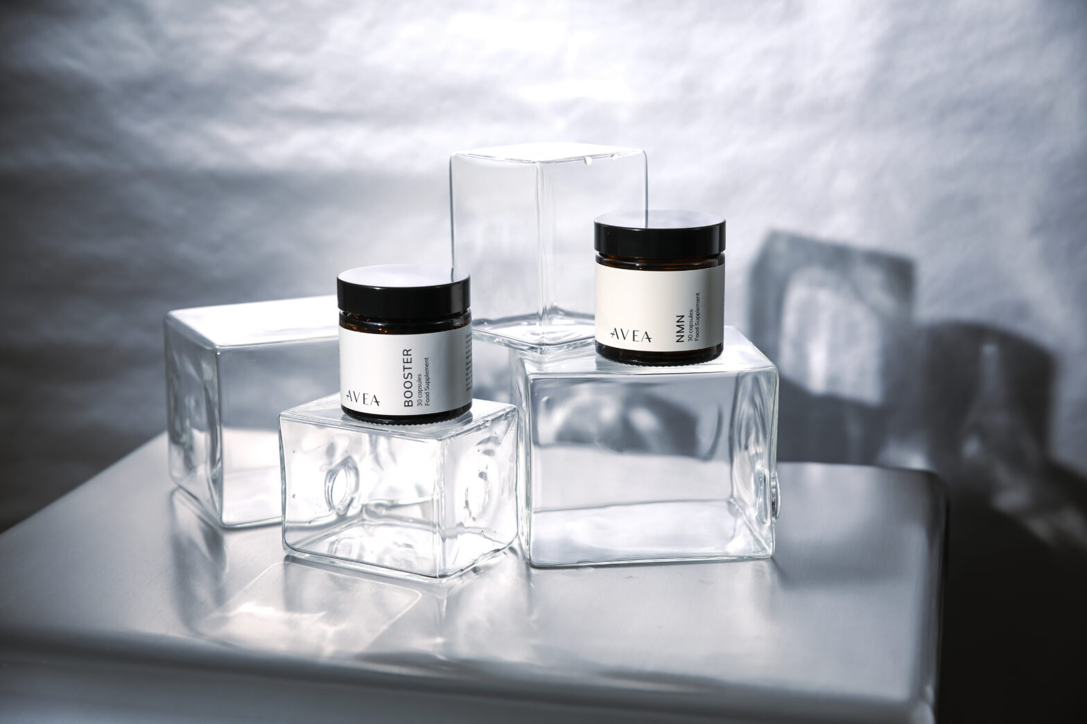 Minimalist product shot of AVEA NMN and Booster supplements displayed on clear glass cubes with soft natural lighting