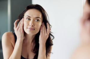 Woman gently touching the sides of her face while looking into a mirror.